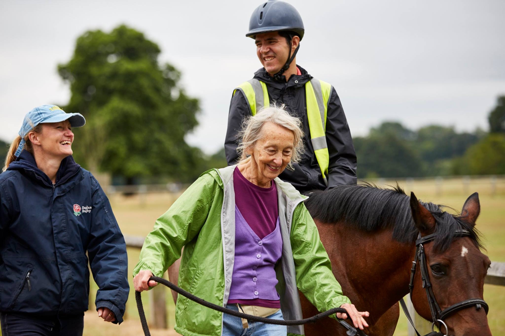 Man on a horse smiling with two ladies walking next to him